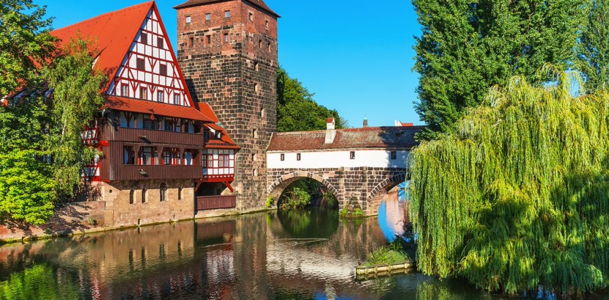 Puente medieval encima de un rio, a un lado casona y torreón medieval de color rojo