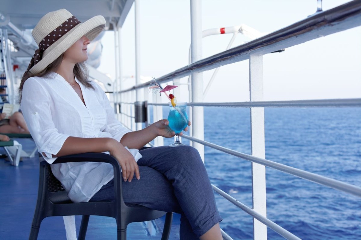 Mujer sentada en la cubierta del barco con un coctel en la mano mirando al horizonte
