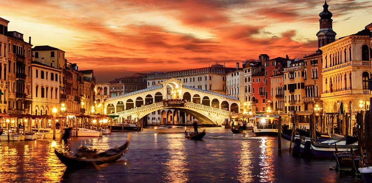 Al atardecer en el Gran Canal donde se ven góndolas y al fondo un puente antiguo