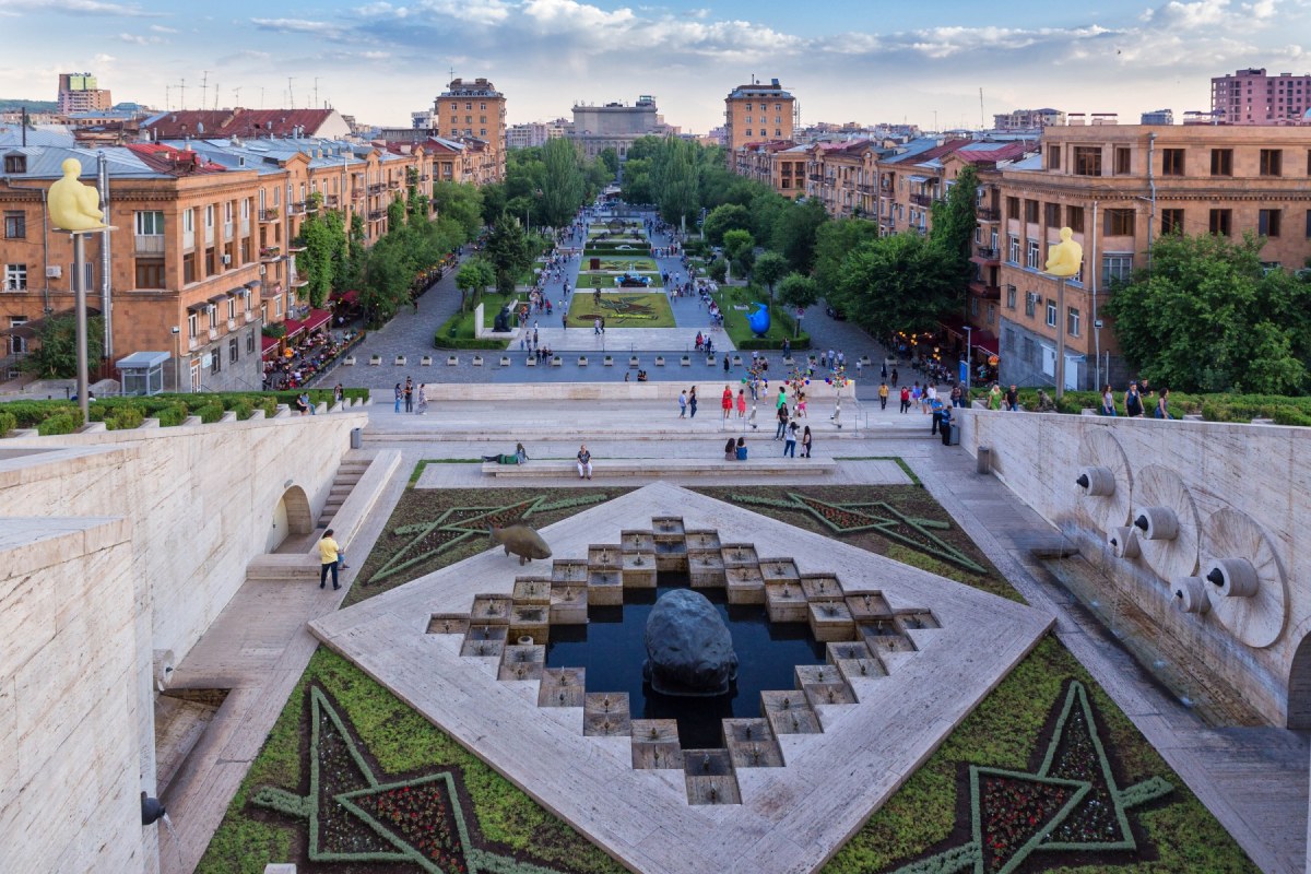 Monumento con una fuente en el medio y al fondo una avenida con casas a sus lados