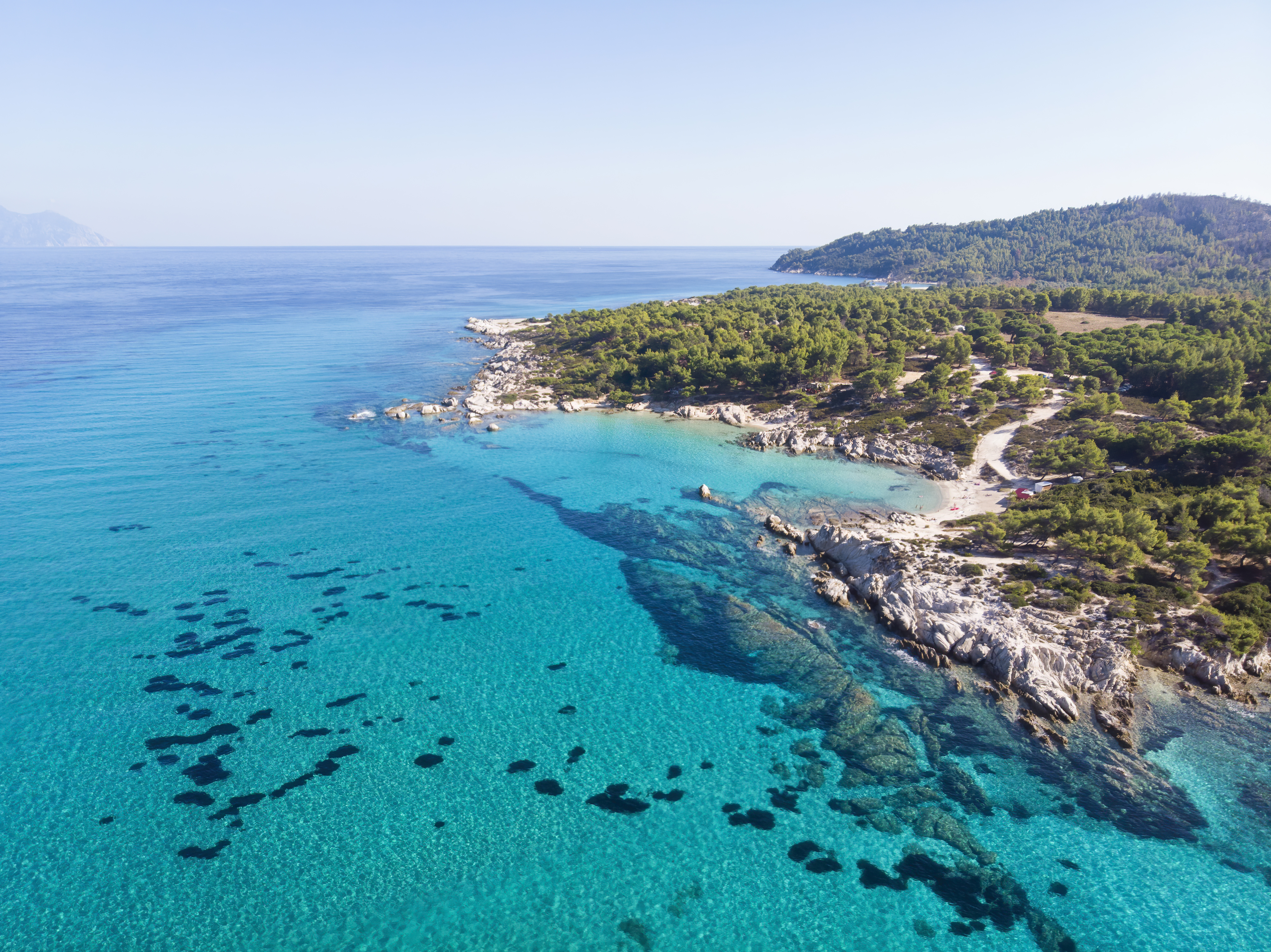 Costa rocosa del mar Egeo en Grecia, con aguas turquesas cristalinas que gradúan del azul profundo al verde claro cerca de la orilla.