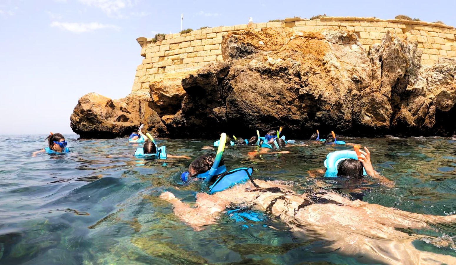 grupo de jóvenes haciendo snorkel al lado de unas piedras en el mar
