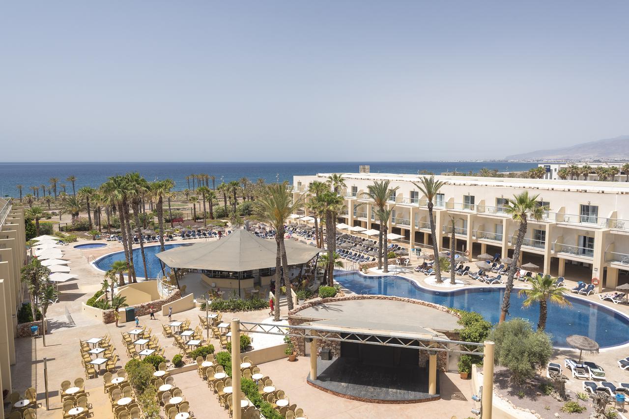 Piscina de un hotel de color blanco con palmeras y al fondo el mar