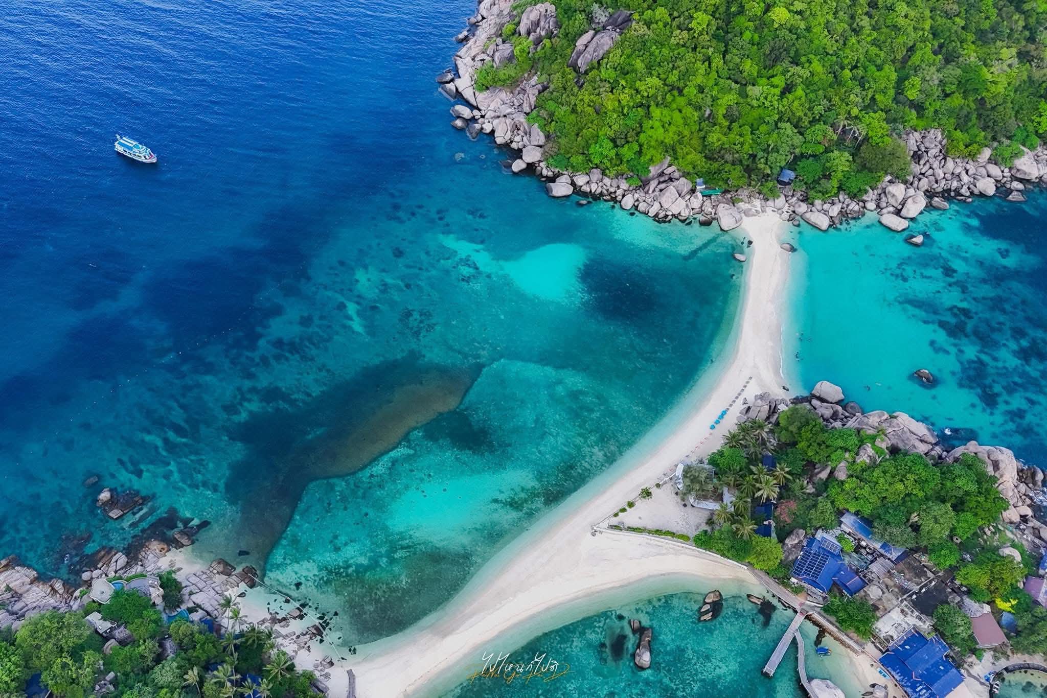 vista aérea muestra una lengua de arena blanca estrecha que conecta dos islotes rocosos en forma de pollo, rodeada de aguas turquesas cristalinas