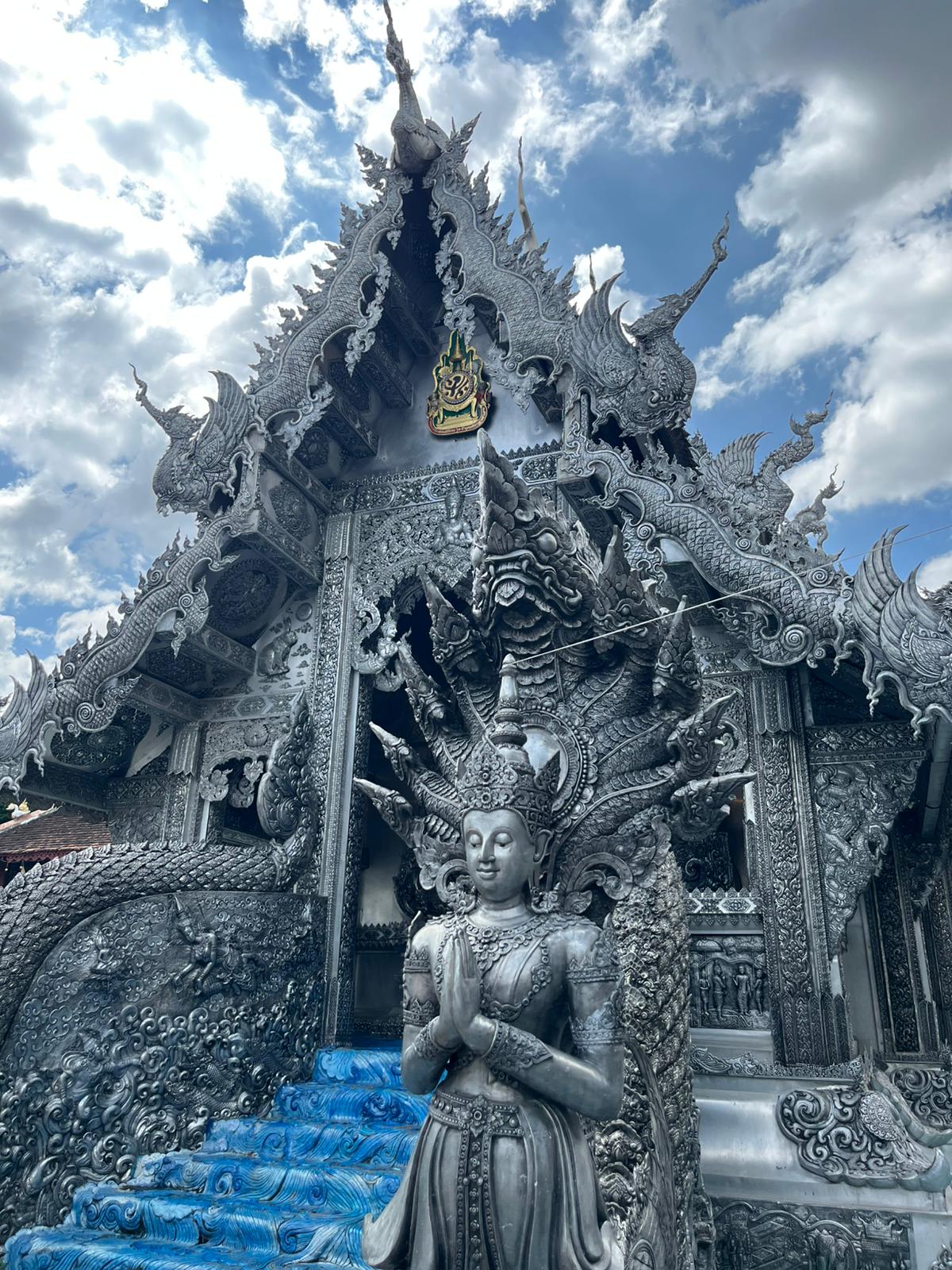 Templo Blanco, Chiang Rai. Fachada blanca brillante con espejos incrustados con serpientes míticas en el techo y una figura femenina blanca orando