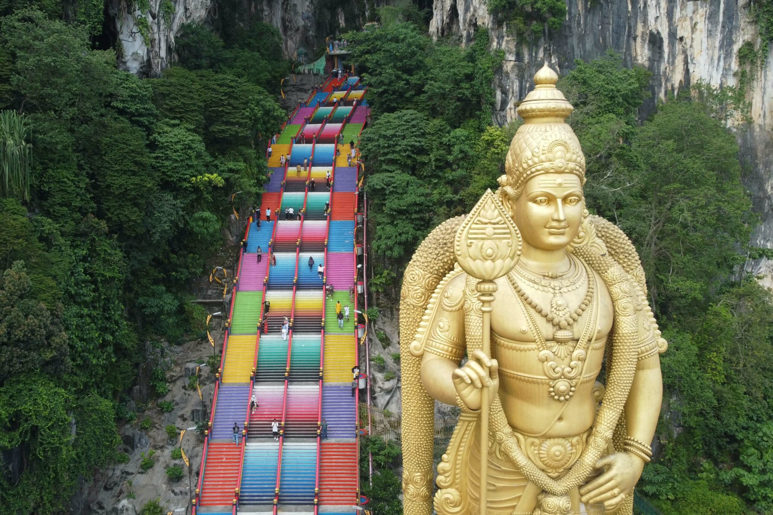 Estatua gigantesca hindú de color oro en una montañas con escaleras de colores a su lado