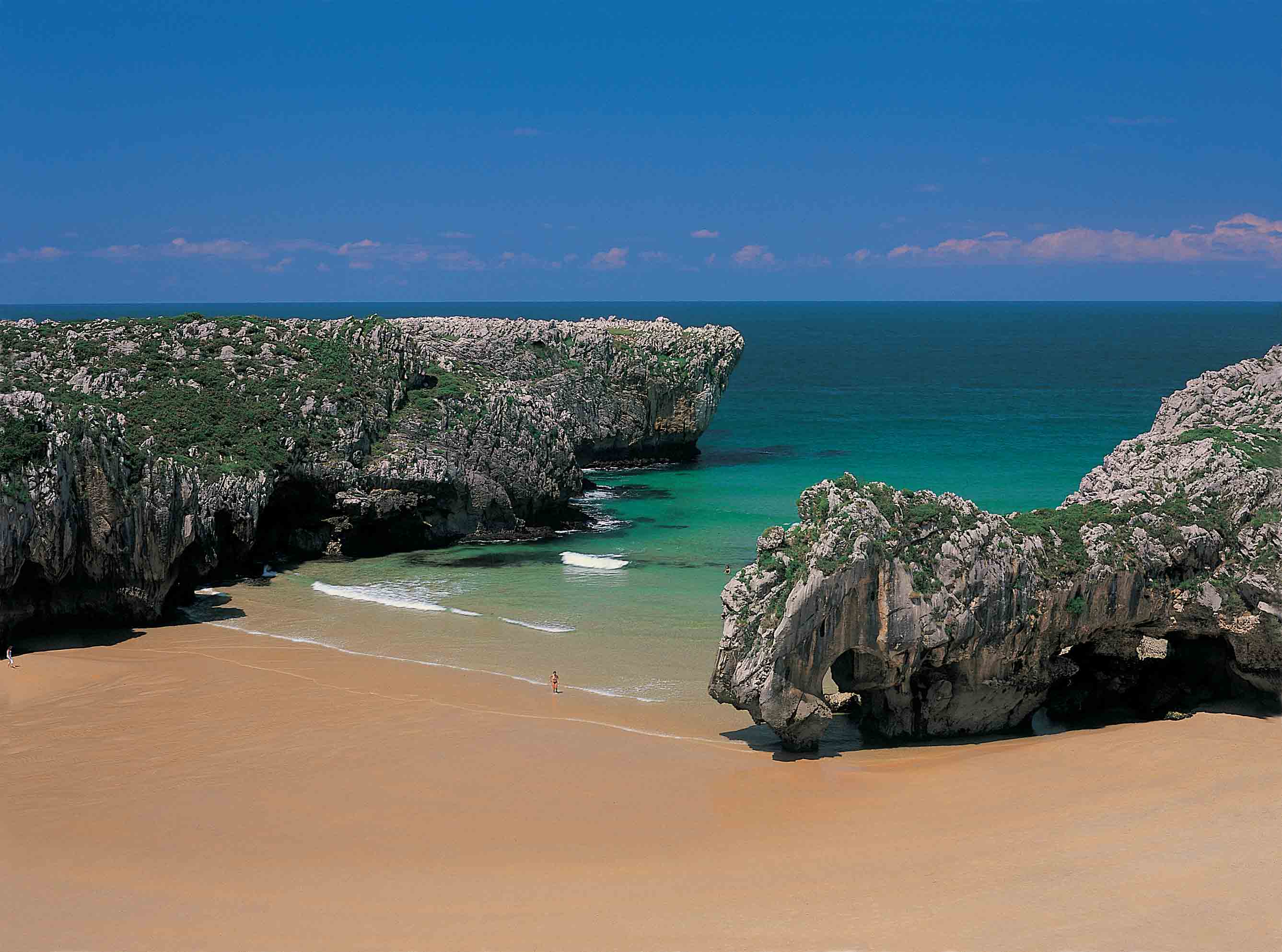 Playa de arena marrón con una entrada de mar entre dos grandes rocas