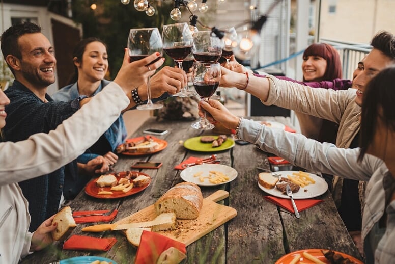 Grupo de personas sentados en una mesa llena de comida y brindando con vino