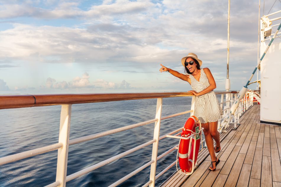 Mujer sonriendo apoyada en la barandilla de la cubierta del barco señalando al horizonte