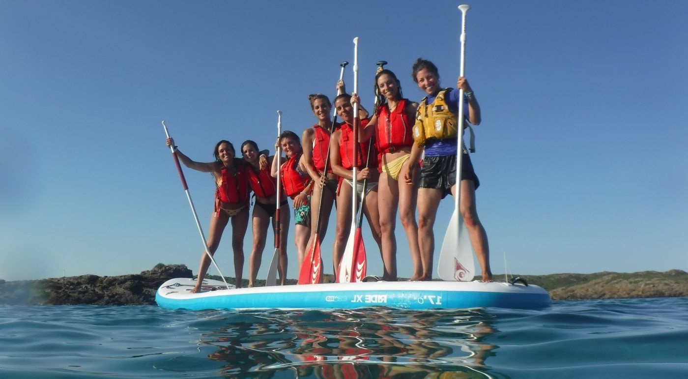 Chicos y chicas montados en una tabla de paddle suft con los remos