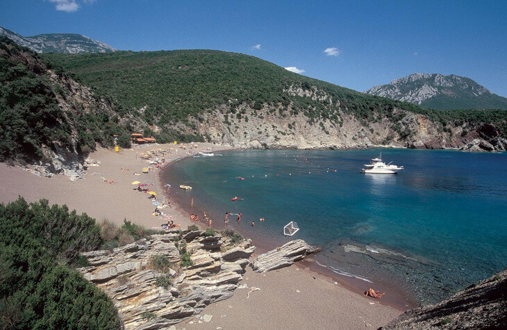 Panorámica de una playa rodeada de montañas y unos yates fondeados en el mar