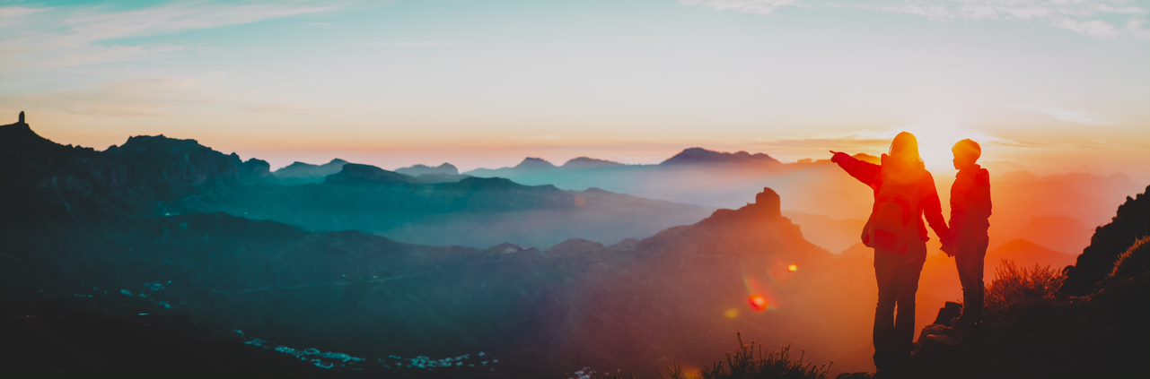 Dos personas de espaldas admirando el paisaje de montañas al atardecer