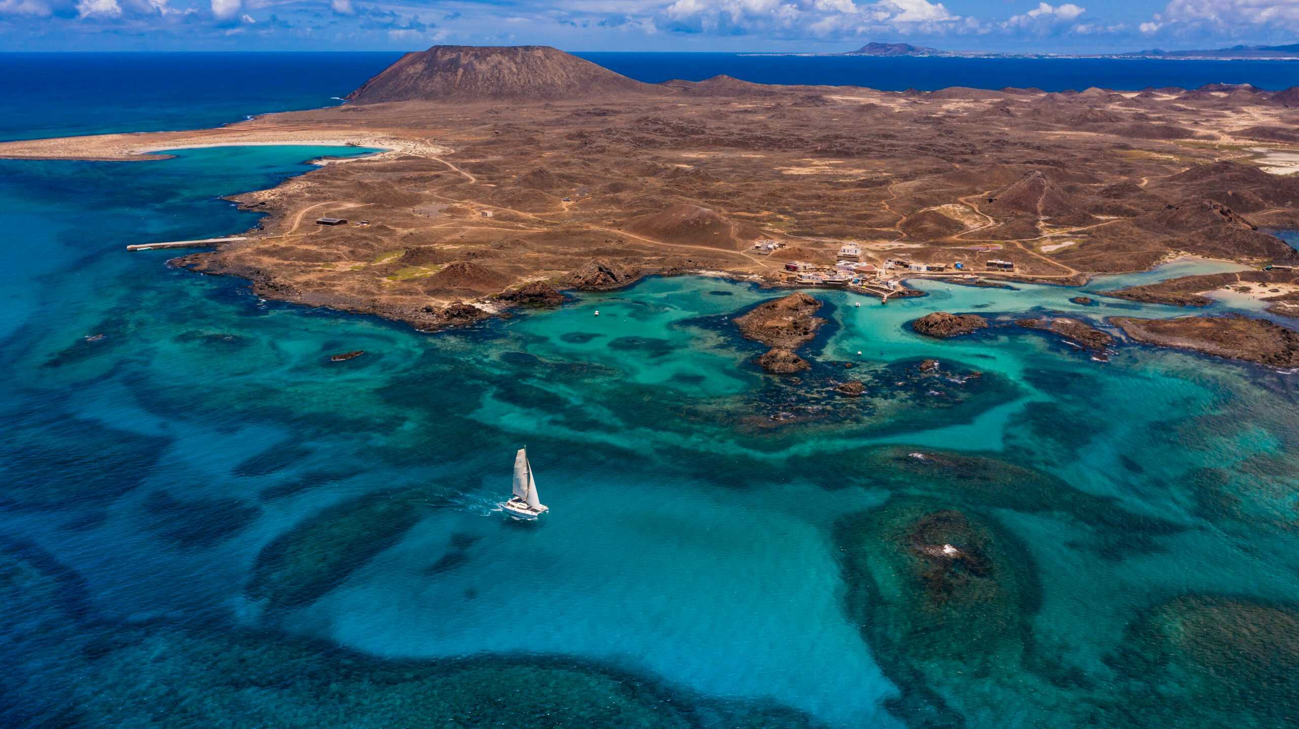 Fuerteventura vista desde el aire donde se aprecia el litoral de aguas cristalinas donde navega un catamarán