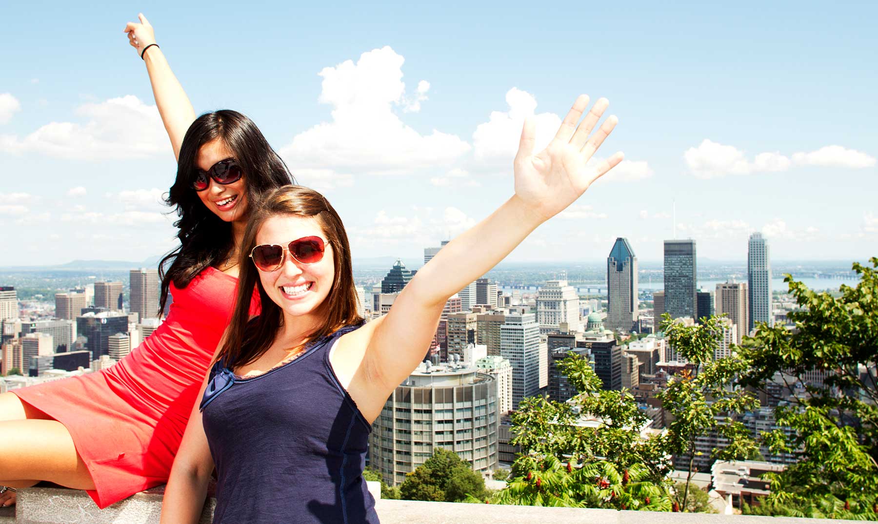 dos chicas posando sonrientes con gafas de sol y brazos alzados detrás la ciudad