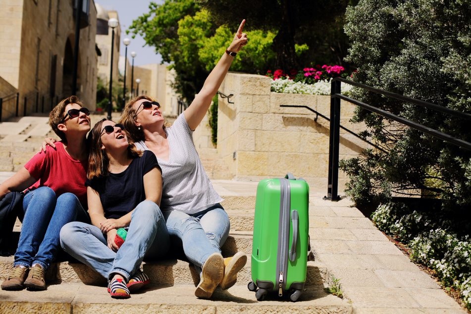 Tras mujeres sentadas en unas escaleras con una maleta haciéndose un selfi