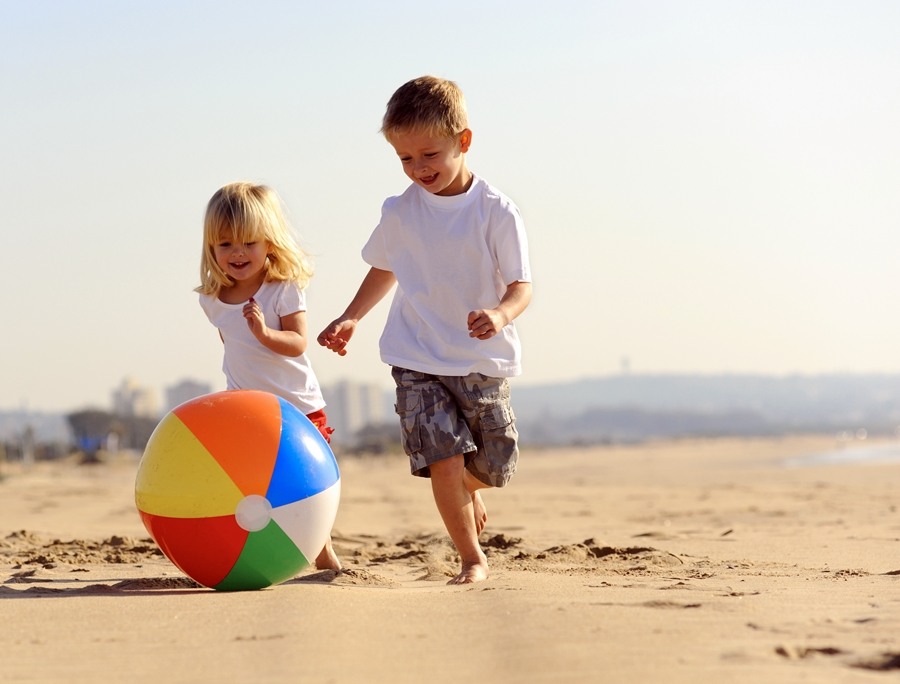 Dos niños pequeños jugando con una pelota hinchable de colores en la playa