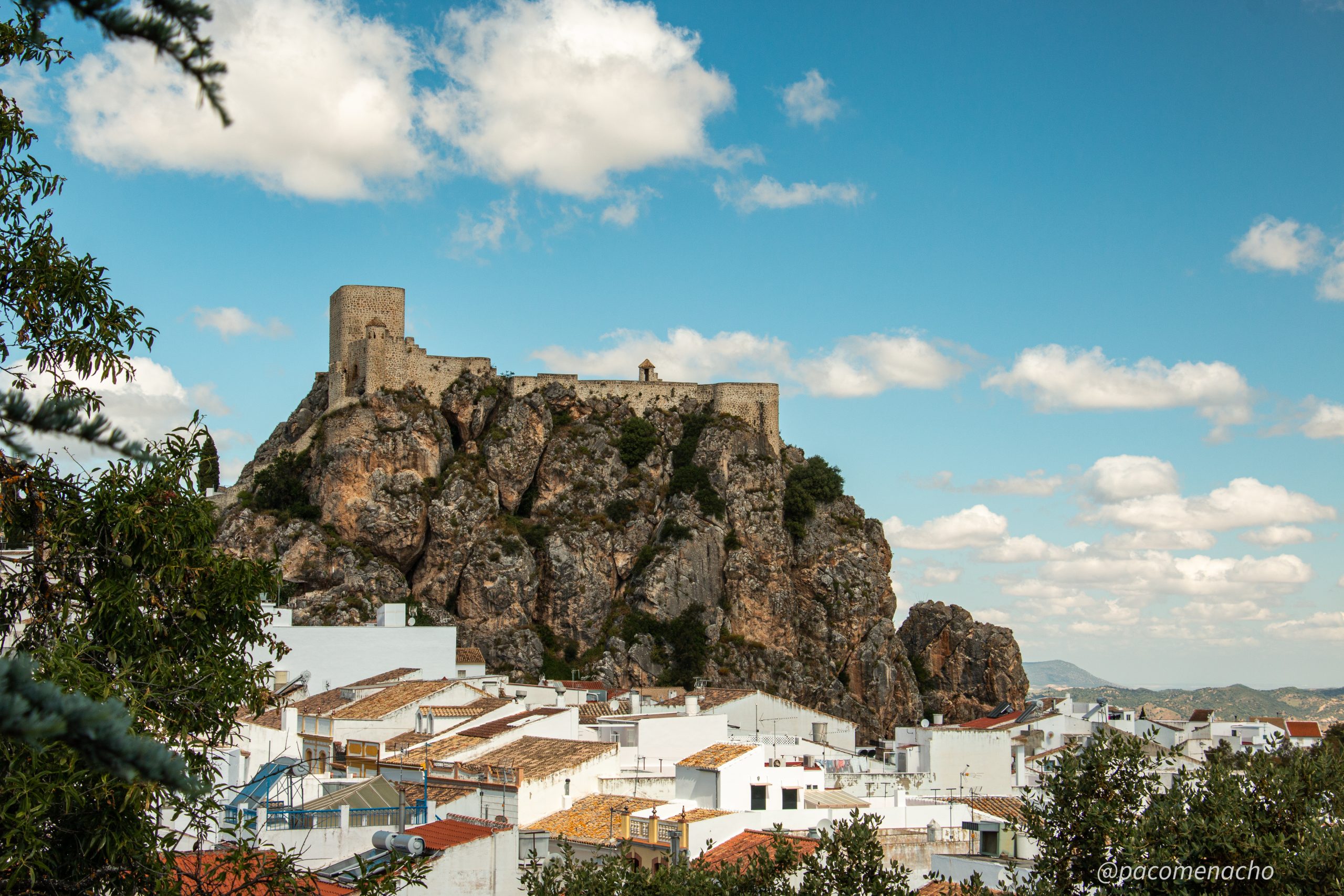 Castillo en el pico de una colina dominando las casas de color blanco abajo