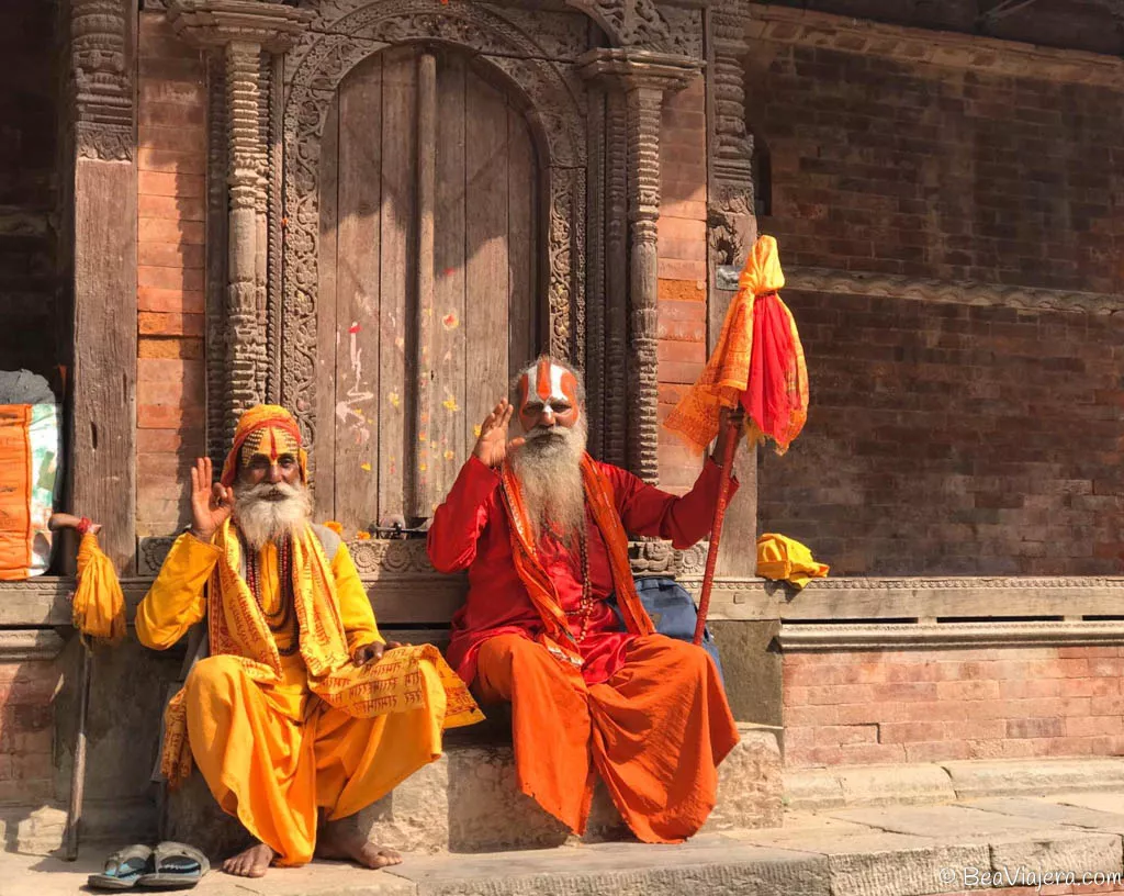 Dos ancianos sacerdotes vestidos de naranja con la cara pintada sentados en un peldaño saludando