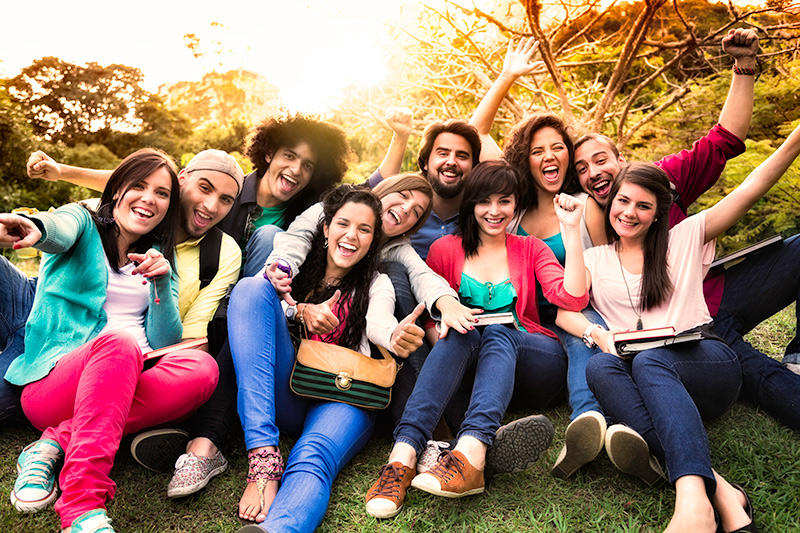 Grupo de chicas y chicos posando sentados en la hierba sonrientes
